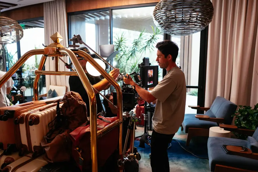 Camera operator filming a hotel lobby set with a gold luggage cart