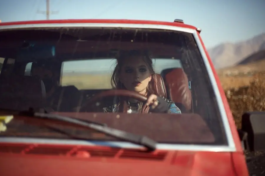 Woman at the wheel of a red truck in the desert, from Desert Sons