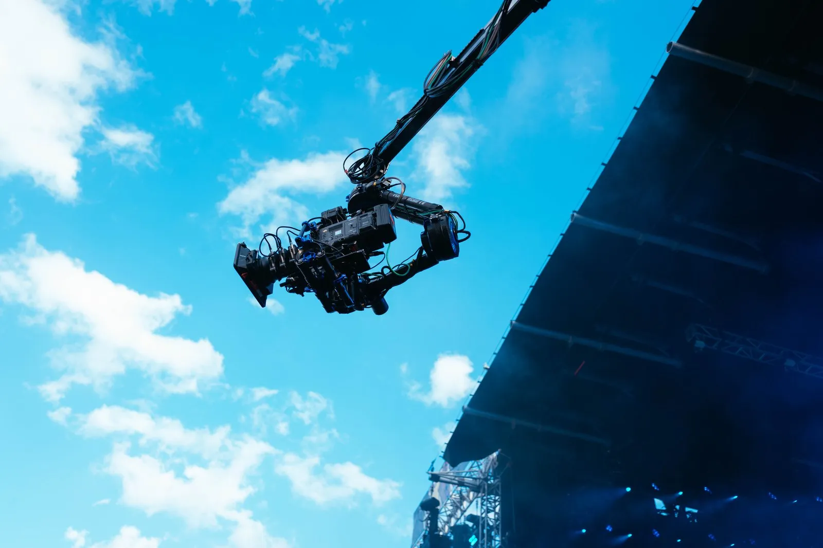 Camera on a jib arm against a blue sky beside a festival stage
