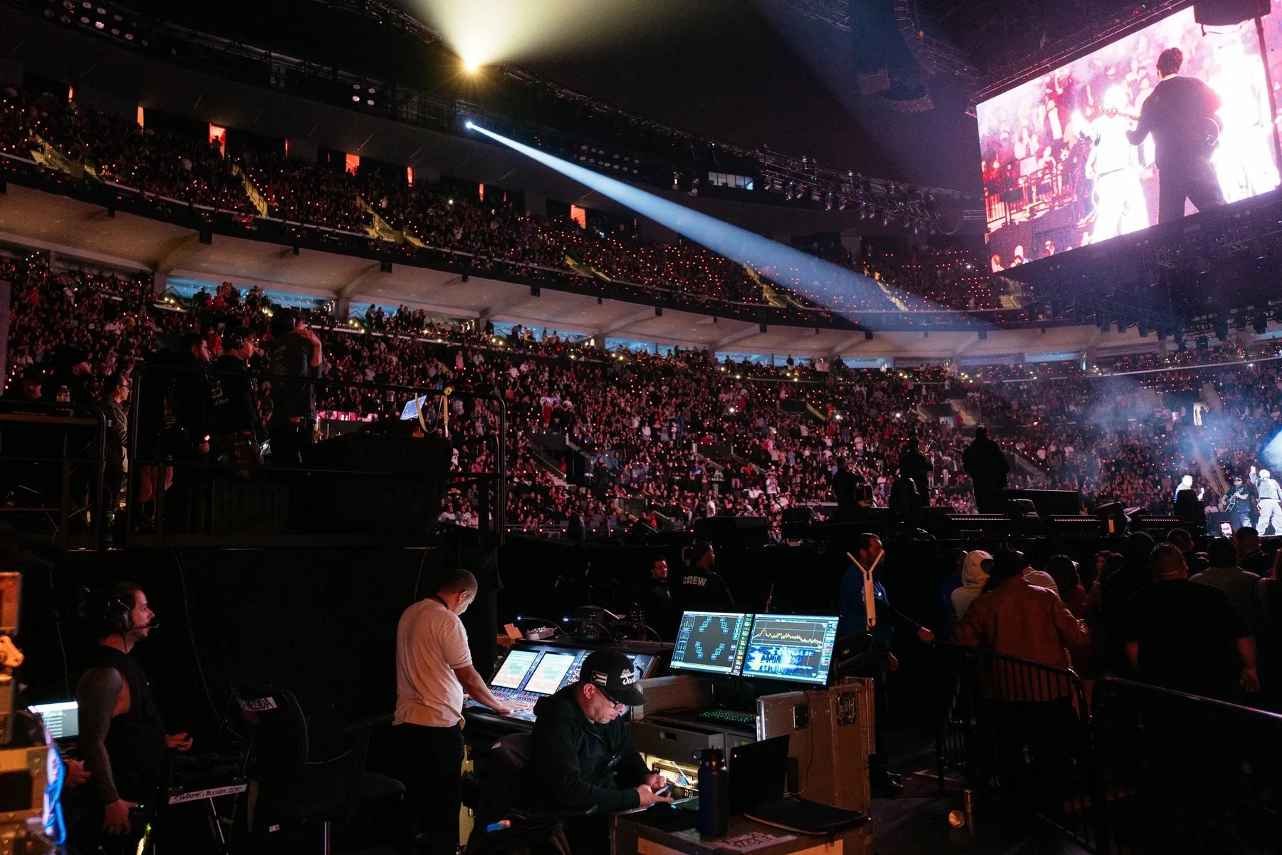 Crew at the broadcast desk on an arena floor, the show playing on the screen above