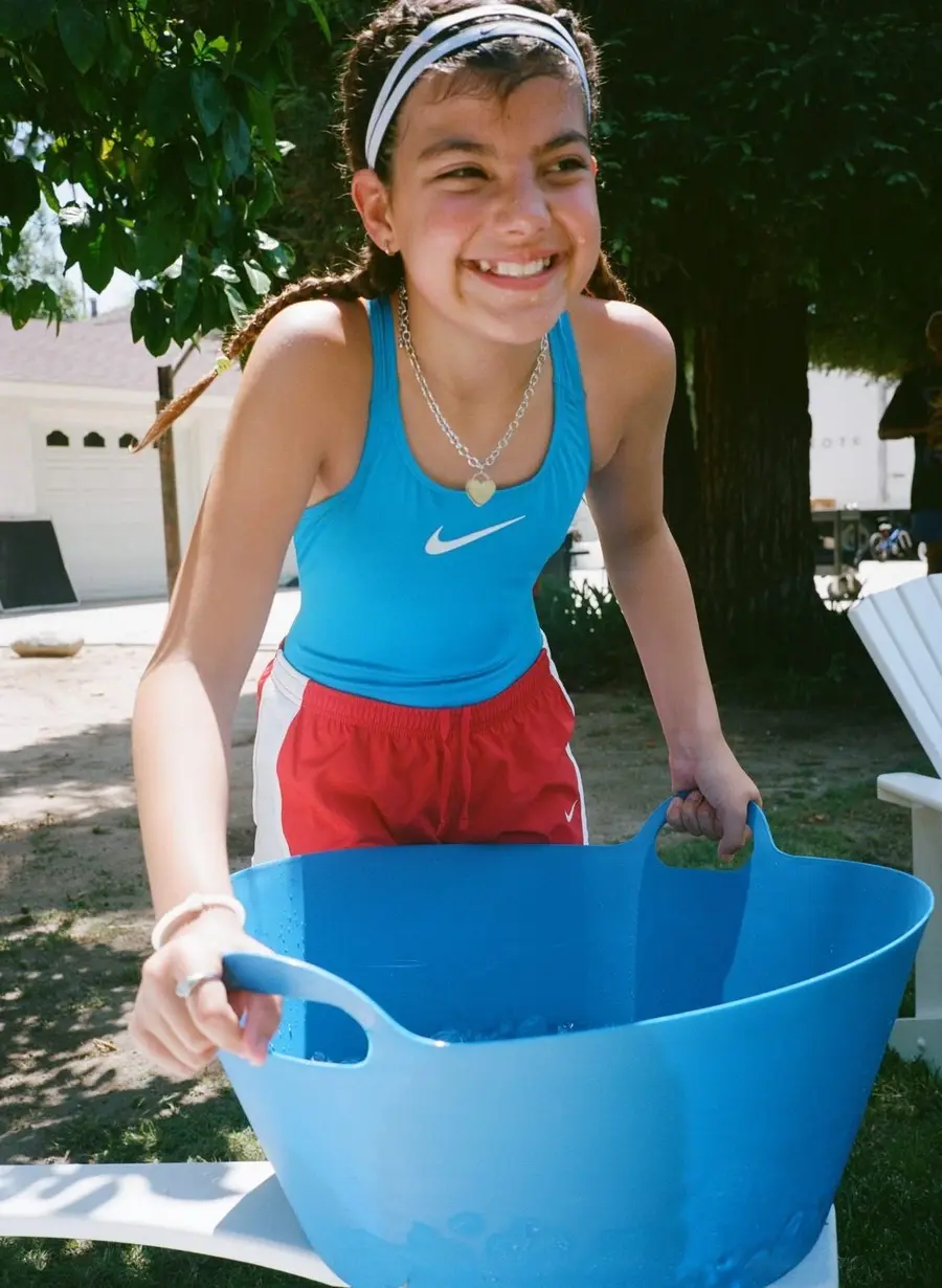 Girl in a blue Nike tank and red shorts holding a blue tub in a backyard