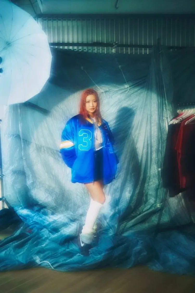 Yoon Ahn in a blue varsity jacket on a teal studio backdrop