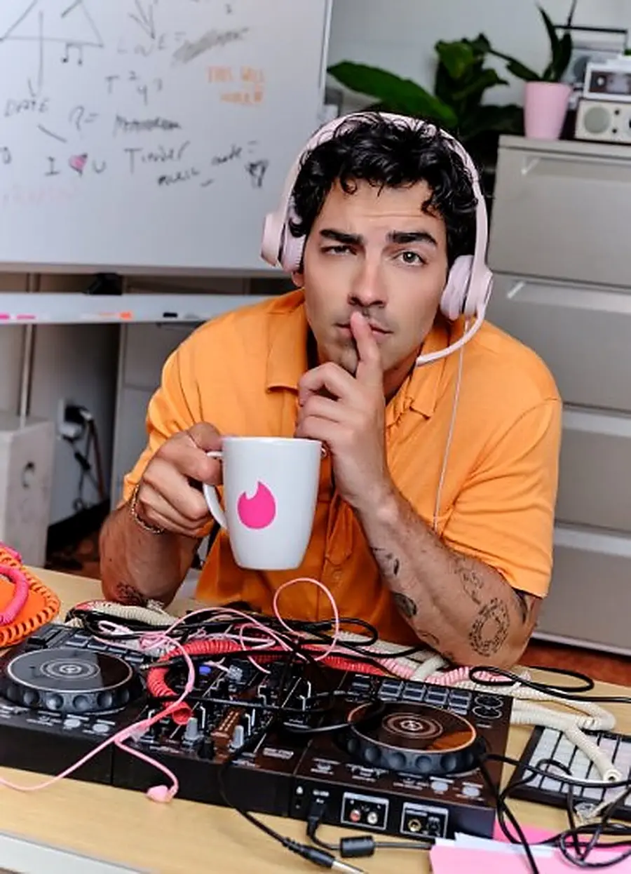Joe Jonas shushing the camera with a Tinder mug and pink headphones