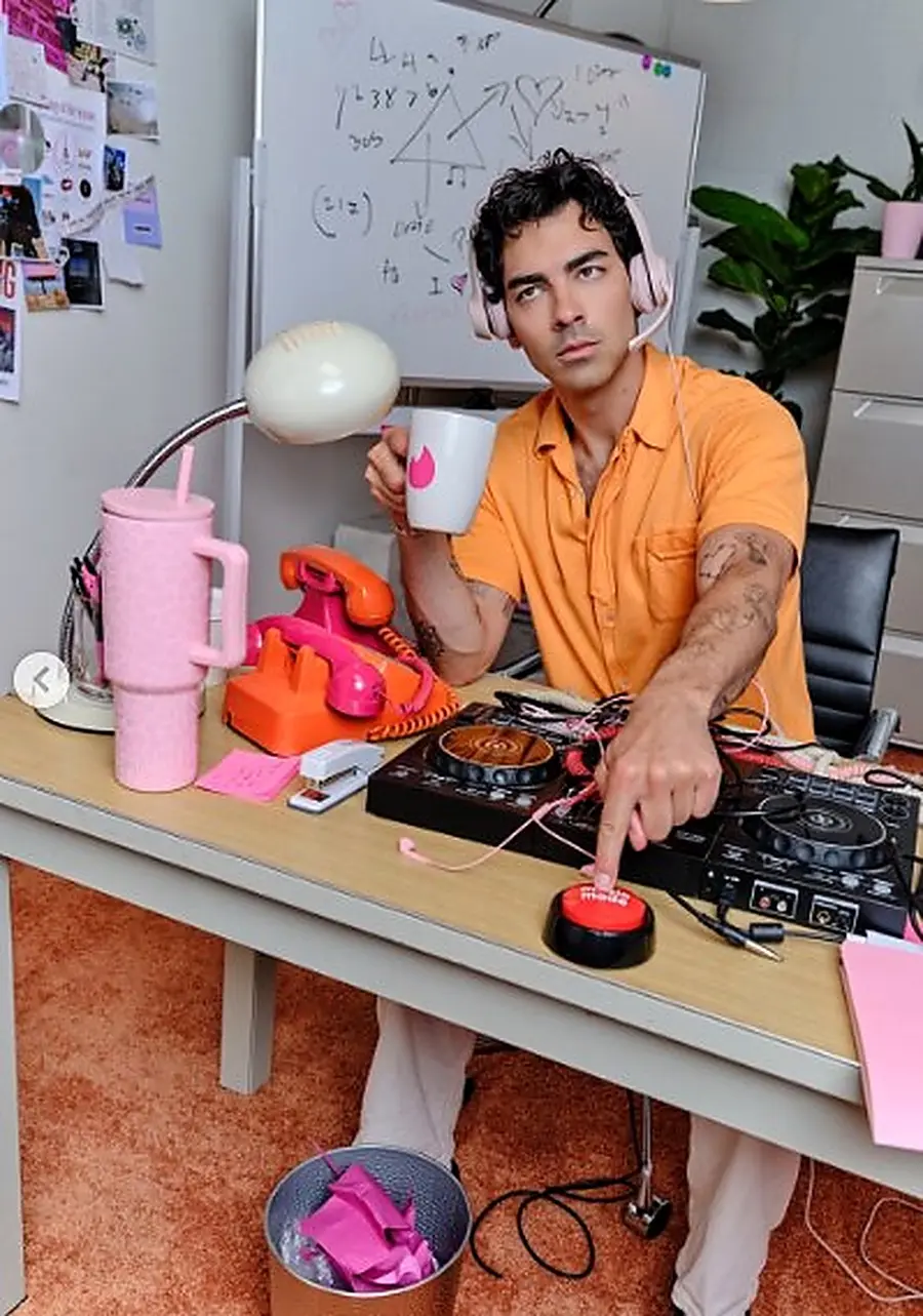 Joe Jonas at the desk hitting a red button, Tinder mug in hand