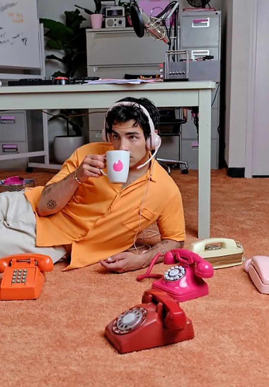 Joe Jonas lying on the orange carpet among vintage telephones